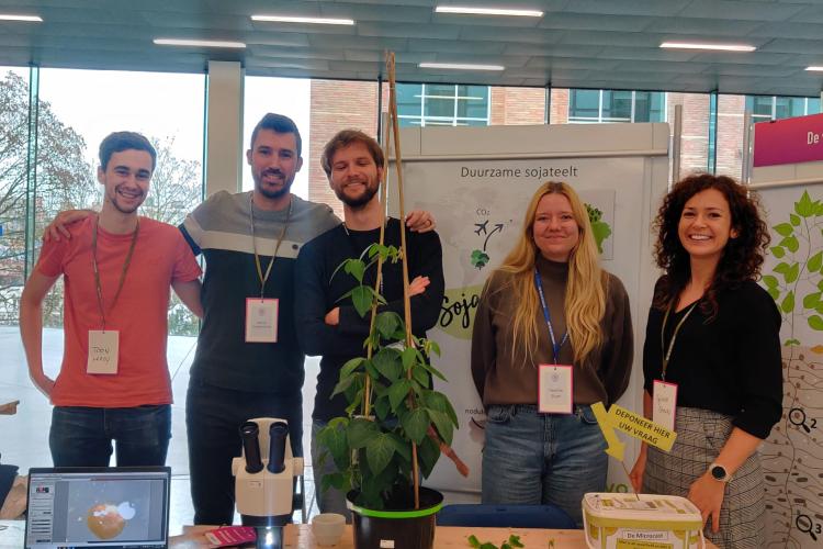 5 people from the Goormachtig lab at dag van de Wetenschap 2023, standing in front of scientific posters and behind a table displaying several plants.